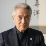 Portrait of an older man wearing a dark traditional-style jacket indoors.